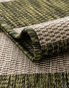 a close up view of a green and beige area rug with an interesting woven design