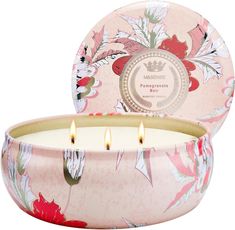 a pink flowered candle with two lit candles in it's center and the lid open