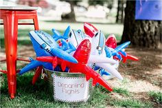 red, white and blue plastic airplanes are in a bucket on the grass next to an orange chair