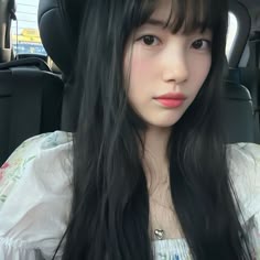 a woman with long black hair sitting in the back seat of a car looking at the camera