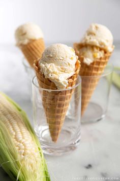 three scoops of ice cream sit in a glass next to an ear of corn