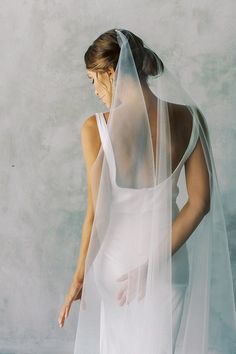 a woman wearing a white wedding dress with a veil on her head and hands behind her back