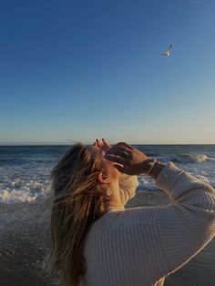 a woman standing on top of a beach next to the ocean holding her hands up