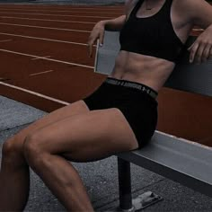 a woman sitting on top of a bench next to a tennis court with her legs crossed