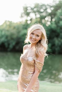 a woman in a gold sequin dress posing for a photo by the water with her hand on her hip