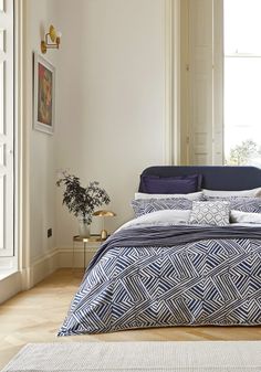 a bed with blue and white comforter in a bedroom next to a plant on the floor