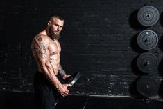 a shirtless man holding a barbell in front of a wall with dumbs