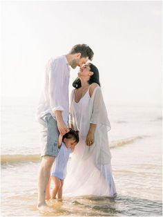 a family standing in the water at the beach, holding hands and looking into each others eyes