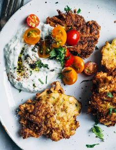 a white plate topped with fried food next to a side of mashed potatoes and tomatoes