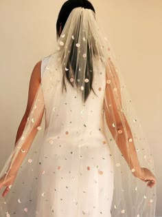 a woman wearing a veil and dress with flowers on it's back, standing in front of a wall