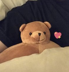 a brown teddy bear sitting on top of a person's stomach in bed with a heart sticker