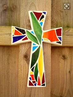 a cross made out of stained glass sitting on top of a wooden fence post with wood planks behind it