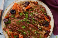 a plate with meat, carrots and onions on it next to a knife and fork