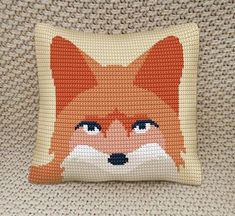 a cross stitch fox pillow sitting on top of a couch