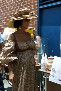 a woman in a dress and hat walking down the street