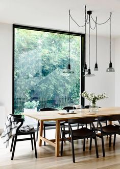 a dining room table and chairs in front of a large window with trees outside it