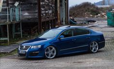 a blue car parked on the side of a road next to a wooden structure and building