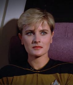 a woman with blonde hair wearing a star trek uniform and looking off into the distance