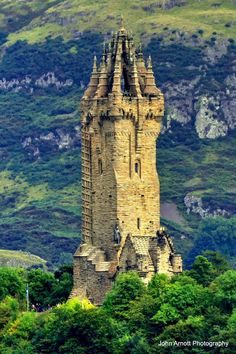 a very tall tower sitting in the middle of a lush green forest covered hillside next to a mountain