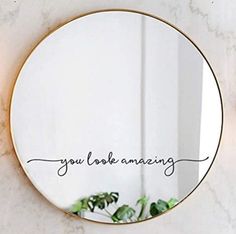 a round mirror with the words you look amazing written in black ink on it next to a potted plant