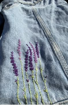 some purple flowers are embroidered on the back of a jean jacket