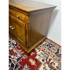 a wooden cabinet sitting on top of a red and blue rug next to a white wall