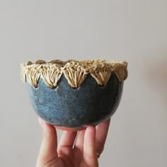 a hand holding up a blue bowl with leaves on it