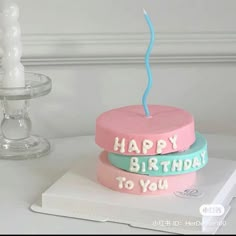 two birthday cakes sitting on top of a white table next to a glass vase and candle