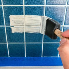 a person holding a paint brush in front of a blue tiled wall with white tiles