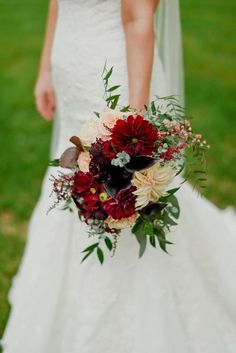 a woman in a wedding dress holding a bouquet with flowers and greenery on it