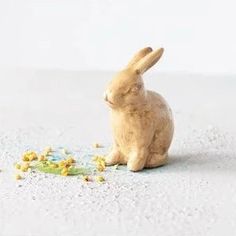 a small wooden bunny sitting on top of a white floor next to yellow and blue flowers