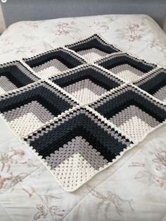 a crocheted blanket is laying on top of a bed with white and black sheets