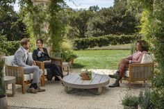 three people sitting in chairs on a patio with potted plants and greenery around them