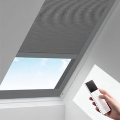 a hand holding a remote control in front of a skylight