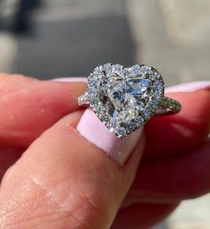 a close up of a person's hand holding a heart shaped diamond ring