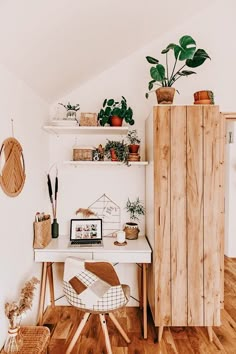 a white desk topped with a laptop computer next to a wooden cabinet and potted plants