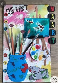 an art journal with paint and brushes in a blue vase on top of a wooden table