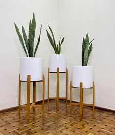 three white planters sitting on top of wooden stands next to each other in a room