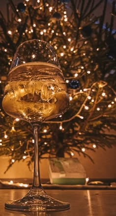 a glass filled with liquid sitting on top of a table next to a christmas tree