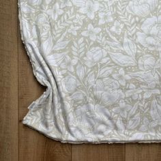 a close up of a white flowered fabric on a wooden floor with wood floors