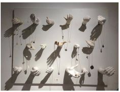 the shadow of several hands and necklaces is cast on a white wall in front of an art work