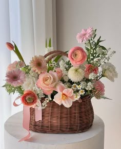 a basket filled with lots of flowers sitting on top of a white table next to a window
