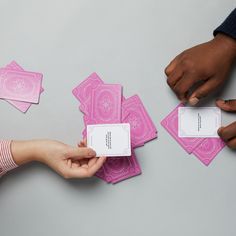 several people are holding pink playing cards on a gray surface with white writing that reads,