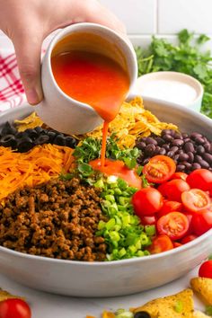 someone is pouring dressing into a bowl full of mexican food, including tortillas and beans