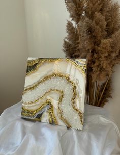 a white and gold marbled box sitting on top of a bed next to dried plants