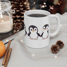 a coffee mug with penguins on it next to some pine cones and cinnamon stickers