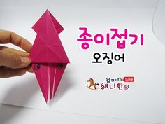 a hand holding a pink origami bird on top of a piece of paper