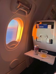 an airplane seat with food and drink on the tray next to it, as seen through the window