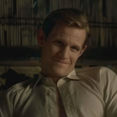 a man wearing a white shirt and tie in front of a book shelf filled with books