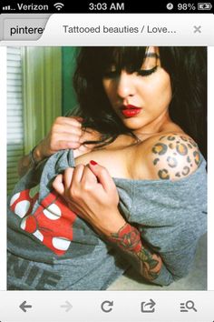 a woman with tattoos on her arm and chest is holding onto a gray shirt that has leopard print on it